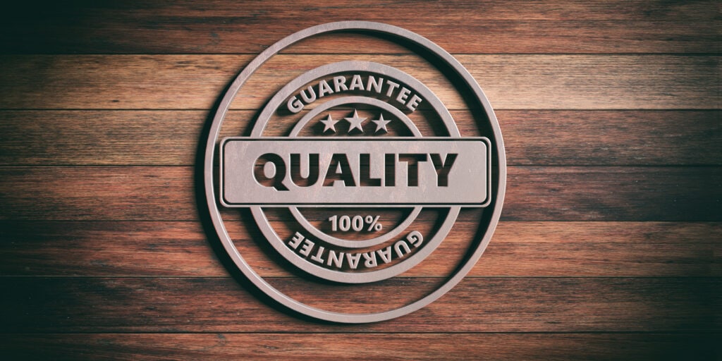 QUALITY badge. Round metal sign with text quality on wooden background. 3d illustration